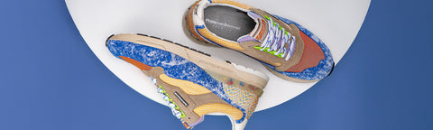 A pair of colorful athletic Floris van Bommel sneakers displayed on a white circular platform against a blue background. The shoes feature a complex, multi-colored design with blue, orange, beige, yellow, green elements.