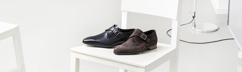 A pair of men's van Bommel shoes, one in black leather and one in brown suede, displayed on a white chair in a minimalist room setting.