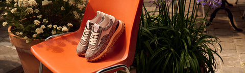 A pair Floris van Bommel sneakers in beige and white, styled on an orange chair outdoors next to potted plants.