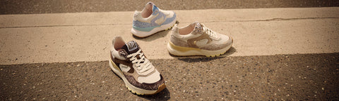 Three Floris van Bommel sneakers arranged on a road surface: one in the foreground with a dark patterned upper, one in the back left with light blue and white panels, and one in the back right with a distressed cream and brown upper.