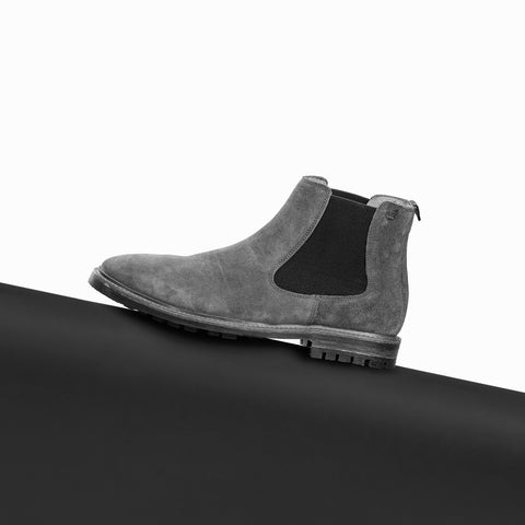 A single grey suede Floris van Bommel Chelsea boot with black elastic side panels, resting on a black surface against a white background.