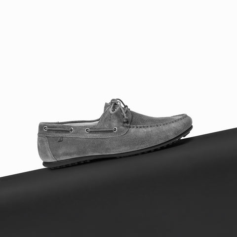 A single grey suede Floris van Bommel boat shoe with laces, positioned on a black platform against a white background.