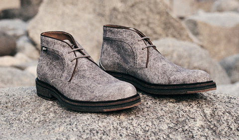 A pair of Floris van Bommel boots with dark brown soles, resting on a textured rock with a blurred rocky background.