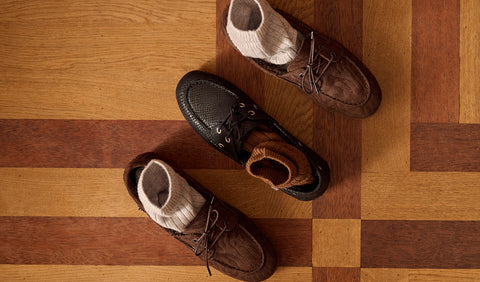 Three pairs of casual lace-up shoes in brown and black, each styled with a white knit sock, arranged on a wooden parquet floor. Floris van Bommel