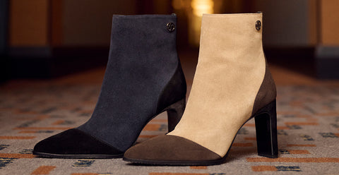Two pointed-toe ankle boots with block heels, shown side by side on a patterned carpet. The boot on the left is dark charcoal grey suede with black toe and heel sections. Floris van Bommel