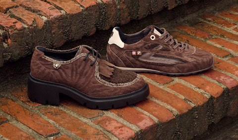 A pair of brown suede Floris van Bommel shoes with fringe detailing and chunky black soles, displayed on a brick ledge.