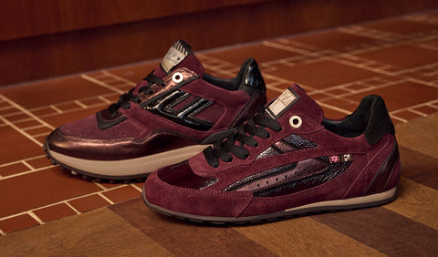 A pair of Floris van Bommel sneakers in burgundy suede and leather with black accents, displayed on a wooden floor.