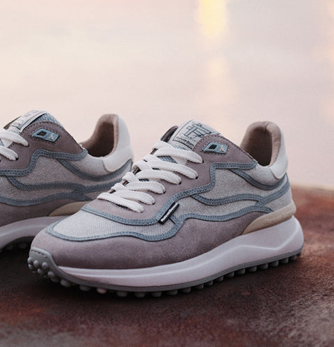 A pair of Floris van Bommel sneakers in grey and light blue suede, with white laces and thick white midsoles, photographed on a textured surface with a soft blurred background.