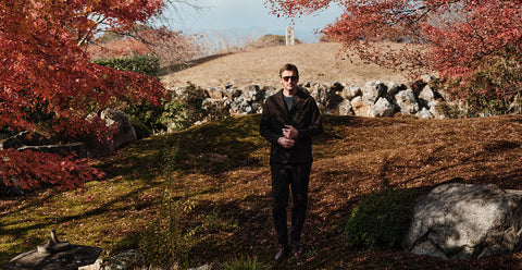 Floris van Bommel wearing a black jacket and dark pants, stands outdoors in a grassy, rocky landscape with red autumn trees on both sides.