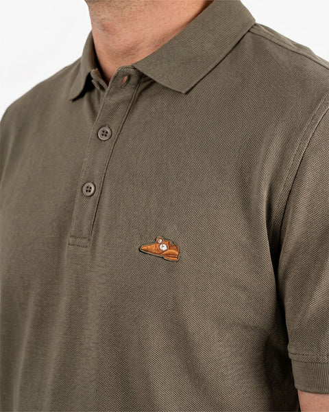 Floris van Bommel. Close-up of a man wearing an olive green short-sleeve polo shirt with a small embroidered patch on the left chest.